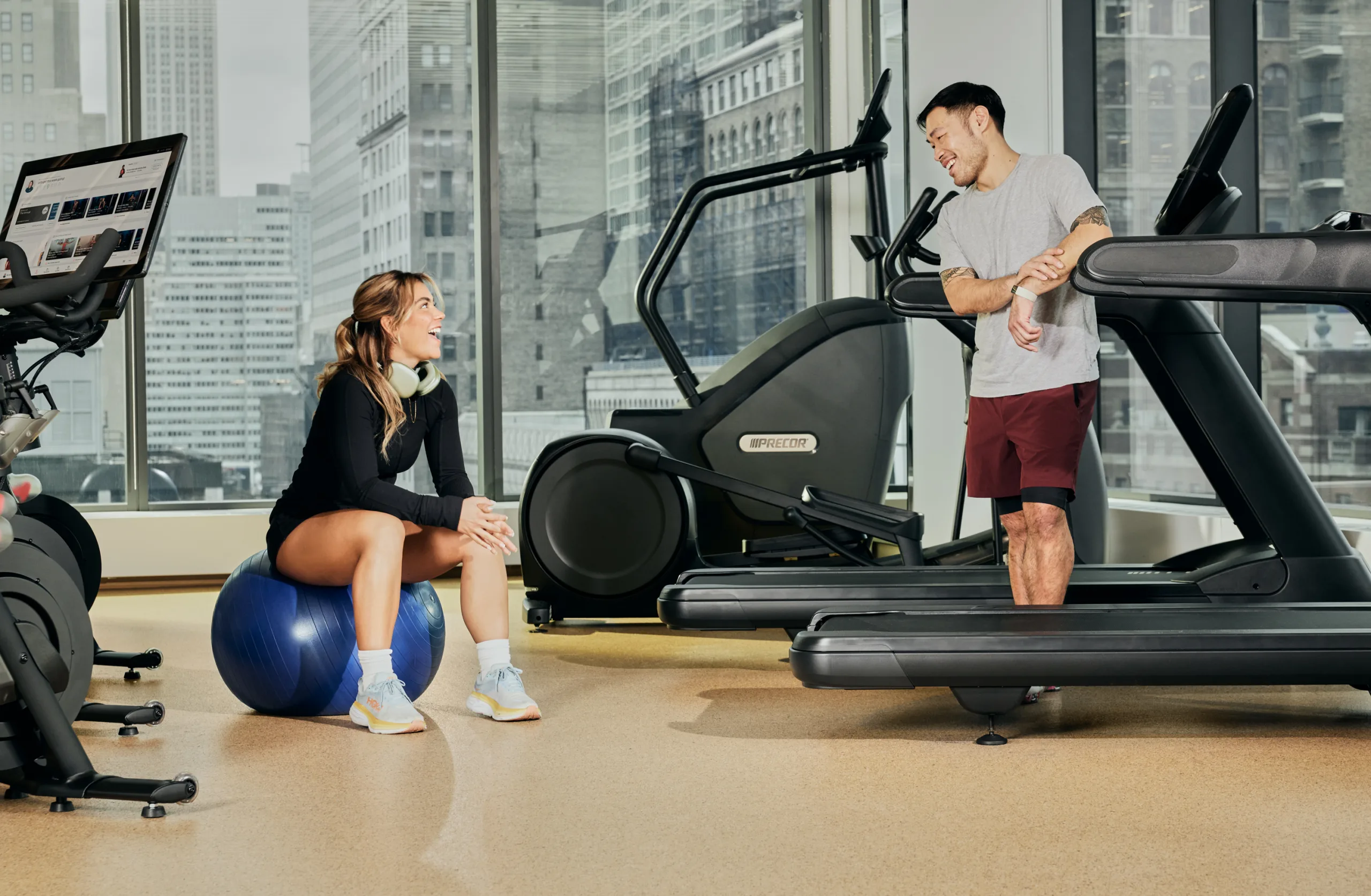 Двое сотрудников общаются после тренировки в светлом корпоративном фитнес-зале, оборудованном кардио-тренажерами Precor.